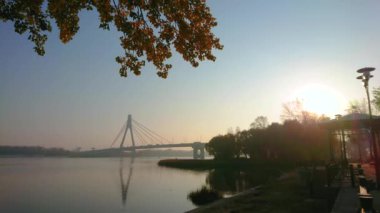 The early morning on Dnieper River with a view on bright sunrise sky, Pivnichnyi (Northern) Bridge and plants in autumn colors, Kyiv, Ukraine