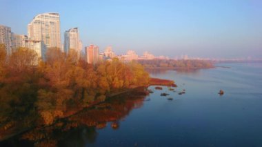 Obolon embankment of Dnieper River with autumn Natalka Park, modern residential high-rises, foggy river surface, Kyiv, Ukraine