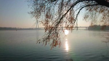 Foggy sunrise on Dnieper River with a view on sun path on the rippled water surface of water and Pivnichnyi (Northern) Bridge in background, Kyiv, Ukraine