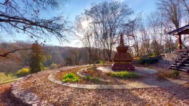 Kuru sonbahar yeşillikleriyle Tibet Bahçesi panoraması, renkli Budist bayrakları, meditasyon için ahşap çarşaf ve arkasında taş ev işi, Kyiv Botanik Bahçesi, Ukrayna