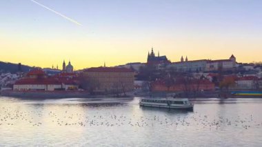 Prag 'da gün batımı zamanı Vltava Nehri, yüzen gemi, sudaki martı sürüsü ve Çek Cumhuriyeti' nin ufuk çizgisine hakim olan Aziz Vitus Katedrali.