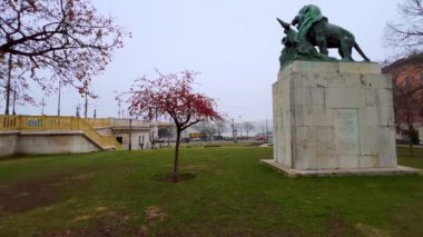 Gyoni Geza Meydanı 'ndaki küçük kış parkında Przemysl Anıtı' nın bronz aslanı, yeşil çimen ve kırmızı meyveler Budapeşte, Macaristan 'daki Çin Yengeç Elması ağacında.