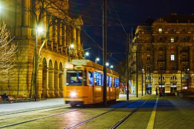 Yellow tram rides on Lajos Kossuth sqaure among nice illuminated buildings, Budapest, Hungary clipart