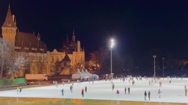 Akşam Şehir Parkı Buz Pisti Panorama 'sında arka planda parlak ışıklar altında güzel Vajdahunyad Şatosu, Budapeşte, Macaristan