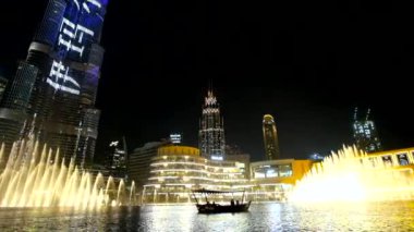 DUBAI, BAE - 3 Mart 2020 'de Dubai Çeşmesi' ndeki hız, Burj Halife ve göldeki küçük turist teknesinin 3 Mart 'ta Dubai' deki ışık gösterisiyle altın ışıkla yükseldi.