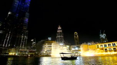 DUBAI, BAE - 3 Mart 2020: Dubai Fıskiyesi 'nin önündeki küçük teknenin siyah silueti, arka planda Burj Halife ışık gösterisi, 3 Mart' ta Dubai 'de