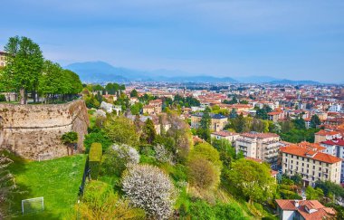 Bergamo Citta Alta tepesinin yamacındaki çiçek açan bahar parkının arka planında Citta Bassa (aşağı kasaba) yaşamaktadır.