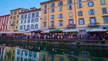 MILAN, ITALY - APRIL 9, 2022: Panorama of Naviglio Grande Canal with crowded embankment, colorful houses, cafes and restaurants at sunset, on April 9 in Milan