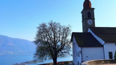 San Martino Kilisesi 'nin dağ yamacındaki panoraması ve Ronco sopra Ascona, Ticino, İsviçre' nin bakış açısından, puslu mavi Maggiore Gölü.