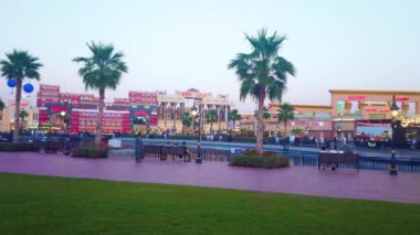 DUBAI, BAE - 6 Mart 2020: Dubai Global Village Dubai 'nin yeşil çimenli, yemyeşil palmiye ağaçları ve ticaret ve sergi pavyonlarının önündeki gölet ortasındaki manzaralı yeşil park, 6 Mart' ta Dubai 'de