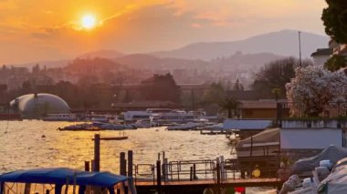 Lugano Gölü 'nün üzerindeki kızgın günbatımı ve Alpler, Lugano, Ticino, İsviçre' nin puslu siluetleri.