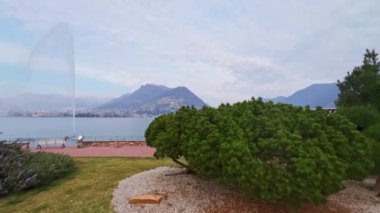 Lugano Körfezi 'ndeki Getto d' Acqua (Su Jeti) Lugano Gölü 'nün arkasındaki kozalaklı parkın arkasındaki çeşme ve çiçek açan biberiye, Lugano, Ticino, İsviçre
