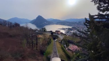 Monte San Salvatore, Ceresio Gölü ve Monte Bre füniküler üzerindeki puslu günbatımı, Monte Bre, Ticino, İsviçre yamacındaki Albonago köyü perspektifinden görüldü.