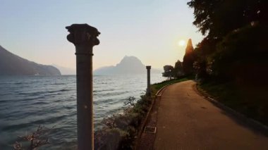 Lugano göl kenarı Park Villa Heleneum 'un üzerinde altın gün batımı. Arka planda taş sütunlar ve Monte San Salvatore manzarası var. Lugano, Ticino, İsviçre