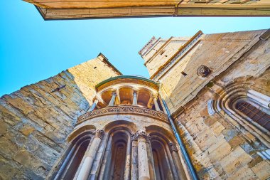 The architectural details of exterior of Basilica of Santa Maria Maggiore, wall columns, portico and carvings of the apse and the tall bell tower with lion's head sculpture, Bergamo, Italy clipart