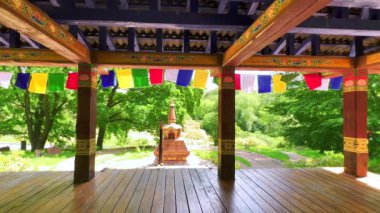 Renkli desenler ve Budist dua bayraklarıyla süslenmiş küçük kırmızı koro ve oyulmuş ahşap çardak Ukrayna 'daki Kyiv Botanik Bahçesi Tibet Bahçesi.