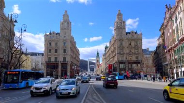 BUDAPEST, HUNGARY - 22 Şubat 2022: Lajos Kossuth Caddesi 'ndeki hız günü trafiği, tarihi konutlar, etkileyici ikiz Clotilde sarayları, Downtown Parish Kilisesi ve Elisabeth Köprüsü, arka planda, Budapeşte, Macaristan