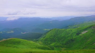 The juicy green valley seen from the peak of Mount Hoverla against the cloudy sky and blue Carpathian mountains in haze, Ukraine