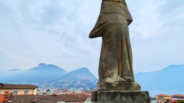 Arka planda San Lorenzo Katedrali, Monte Bre ve Monte Boglia, Lugano, Ticino, İsviçre 'de heykel üzerinde hızlı koşan bulutların zamanlaması