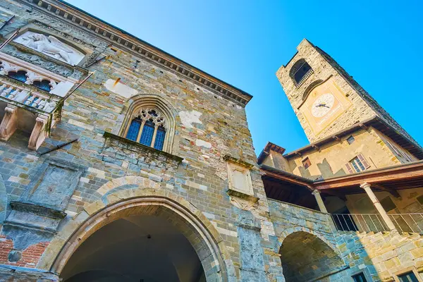 stock image The medieval clocktower of Palazzo della Podesta and the white carved Winged Lion wall sculpture on the wall of Palazzo della Ragione, Piazza Vecchia, Citta Alta, Bergamo, Italy