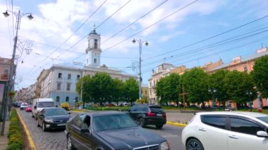 CHERNIVTSI, UKRAINE - 16 Temmuz 2021: 16 Temmuz 'da Chernivtsi' de belediye binasının yüksek kulesi ve önünde yeşil bahçe bulunan Merkez Meydanı boyunca trafik