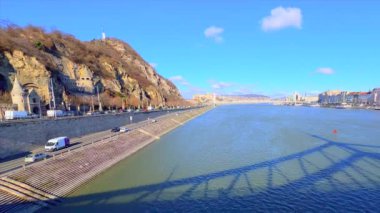 The shadow of Liberty Bridge on the surface of Danube River with Gellert Hill, Pauline Monastery and fast traffic on Szent Gellert embankment, Budapest, Hungary