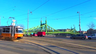 Budapeşte, Macaristan 'daki ikonik yeşil Özgürlük Köprüsü' ne karşı Gellert Meydanı 'nda klasik sarı tramvaylı hızlı trafik