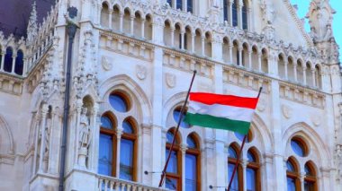 Closeup carved and sculptured Gothic exterior of Parliament with waving National Flag of Hungary, Budapest