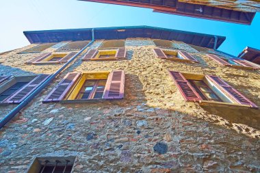 Pencerelerinde kırmızı ahşap panjurlar olan ortaçağ taşından ev manzaralı Carona, Ticino, İsviçre