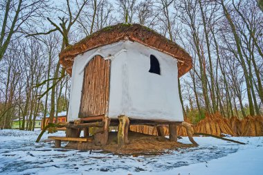 The old adobe stilt house in winter forest of Pereiaslav Scansen, Ukraine clipart