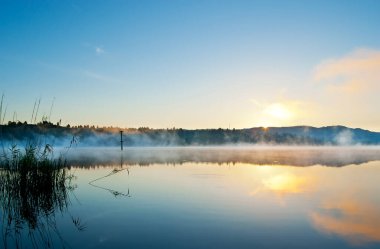 Güneşin baş döndürücü yükselişi, buharlı Mladost Gölü, Veles, Kuzey Makedonya 'nın kristal berrak sularını yansıtıyor