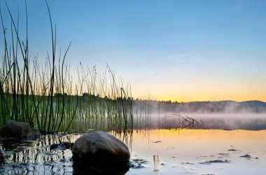 Aynanın düşük açılı görüntüsü Mladost Gölü 'nün yüzeyi gibi, gündoğumu gökyüzü Veles, Kuzey Makedonya' yı yansıtıyor