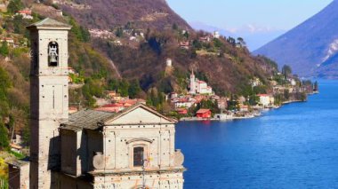 Ortaçağ Santa Maria Annunciata Kilisesi, Albogasio Inferiore 'a karşı San Mamete köyü konutları ve İtalya' nın Valsolda Gölü 'nün parlak mavi yüzeyi.