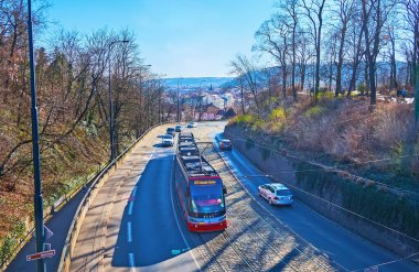 PRAGUE, CZECHIA - MARCH 8, 2022: The busy traffic on Chotkova Street, surrounded with spread old trees of the Chotek Gardens, Prague, Czechia clipart