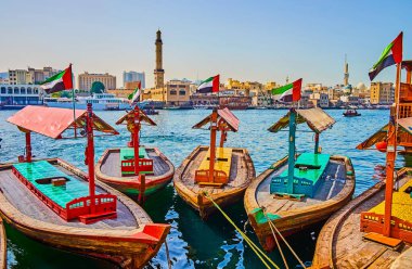 Eski ahşap abra tekneleri Deira ilçesindeki Dubai Deresi 'nin kıyısında demirli; Büyük Cami ve Bur Dubai evlerinin minaresi arka planda, Dubai, BAE