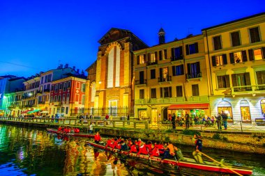 MILAN, ITALY - 08 Nisan 2022: 8 Nisan 'da İtalya' nın Milano kentinde, Naviglio Grande 'deki şehir ışıklarının yansımaları arasında kanal boyunca yavaşça süzülür.