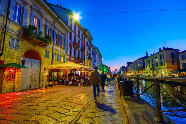 MILAN, ITALY - 08 Nisan 2022: Akşam çökerken, yerel halk ve turistler 8 Nisan 'da İtalya' nın Milano kentinde Naviglio Kanalı boyunca gezintiyi paylaşıyorlar.