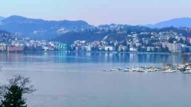 Monte Bre bayırı manzaralı dağ manzarası, Lugano Gölü kıyısında küçük evler ve tekneli tersaneler, Lugano, Ticino, İsviçre