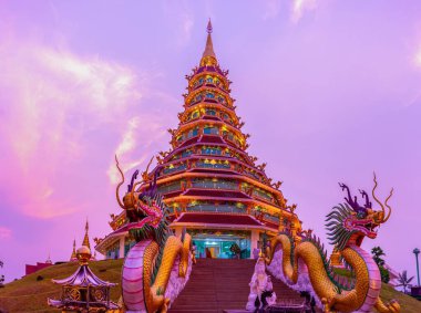Altın Phop Chok Dhamma Chedi alacakaranlık gökyüzünde zarafetle ve simetriyle parıldıyor, Tayland dini mimarisinin özünü yakalıyor, Wat Huai Pla Kang, Chiang Rai, Tayland