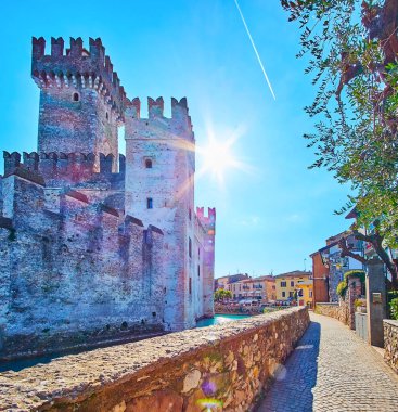 Dante caddesinde yürürken ortaçağ Scaligero Caslte manzarası ve etrafında gök mavisi hendekler, Sirmione, İtalya