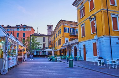 DESENZANO DEL GARDA, ITALY - 10 Nisan 2022: Piazza Cappelletti üzerinde akşam gökyüzü yerel market ve renkli evler tezgahlarıyla, 10 Nisan 'da Desenzano del Garda' da