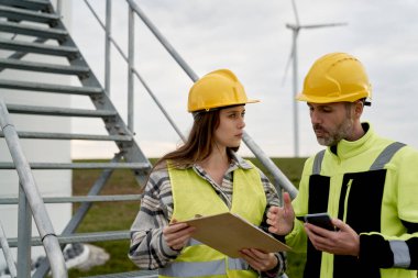 Kafkas erkek ve kadın mühendisler rüzgar türbini sahasında duruyor ve tartışıyorlar. 