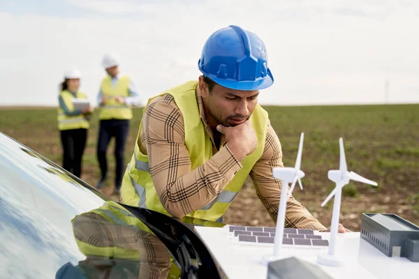 拉丁男性工程师站在风力涡轮机场 靠在车篷上 检查塑料模型 — 图库照片