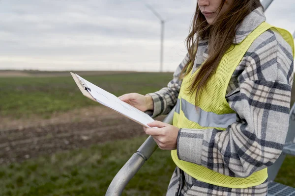 Beyaz Kadın Mühendis Elinde Belgelerle Rüzgar Türbini Sahasında Duruyor — Stok fotoğraf