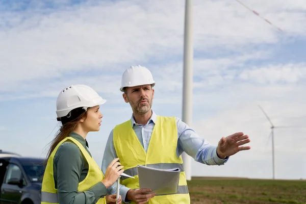 两名高加索工程师站在风力涡轮机场讨论文件 — 图库照片