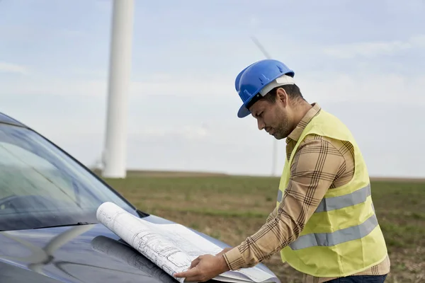 拉丁男性工程师站在风力涡轮机场 检查汽车罩的纸张项目 — 图库照片