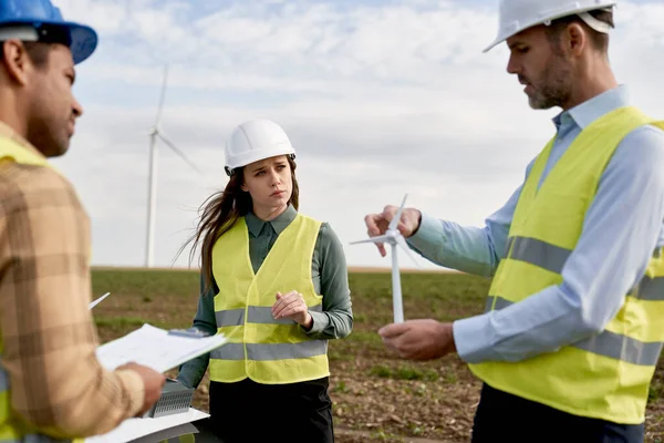 一队高加索和拉丁工程师站在风力涡轮机场 讨论塑料模型 — 图库照片