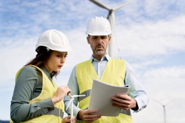 İki Kafkas mühendisi rüzgar türbini sahasında duruyor ve belgeleri tartışıyorlar. 