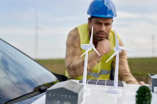 拉丁男性工程师站在风力涡轮机场 靠在车篷上检查塑料模型 — 图库照片