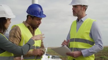 Beyaz ve Latin mühendislerden oluşan bir ekip rüzgar türbini sahasında duruyor ve plastik modeller üzerinde tartışıyorlar. 8K 'da kırmızı helyum kamerayla çekildi..  